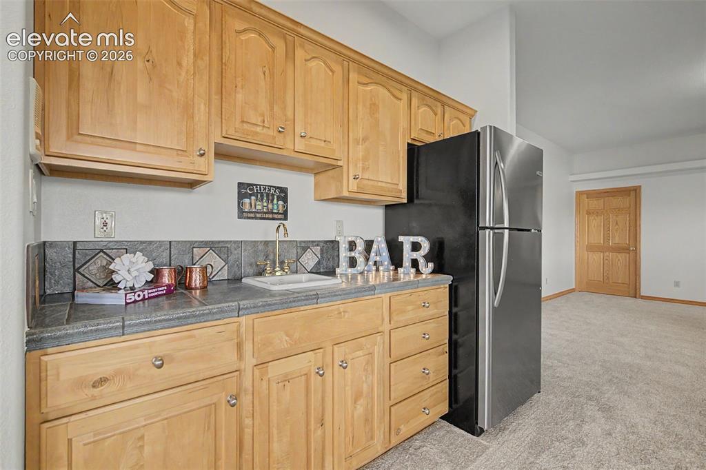 Image 34 of 50: Wet bar featuring wood-finish cabinetry, tile countertop, and a stainless s