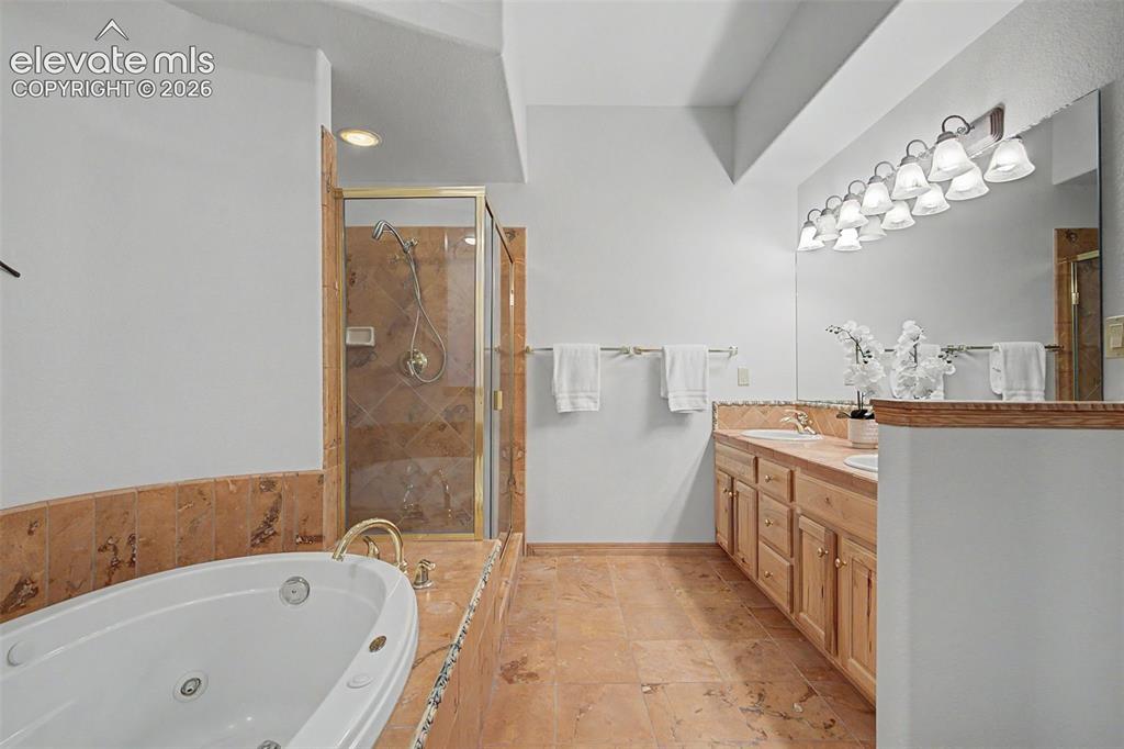 Image 39 of 50: Spacious bathroom featuring a jetted soaking tub, a stand-up shower with gl