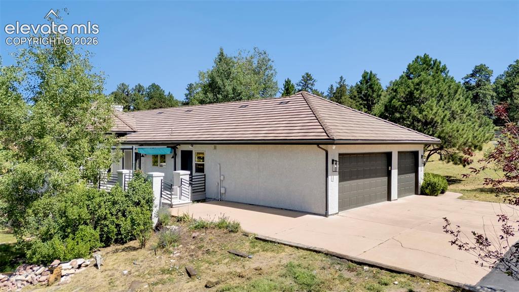 Image 46 of 50: Stucco exterior with a tiled hip roof, featuring a two-car garage with dark