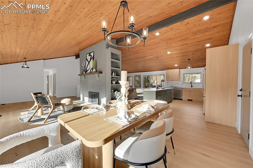 Image 10 of 40: Dining room with light wood finished floors, a fireplace, wood ceiling, and