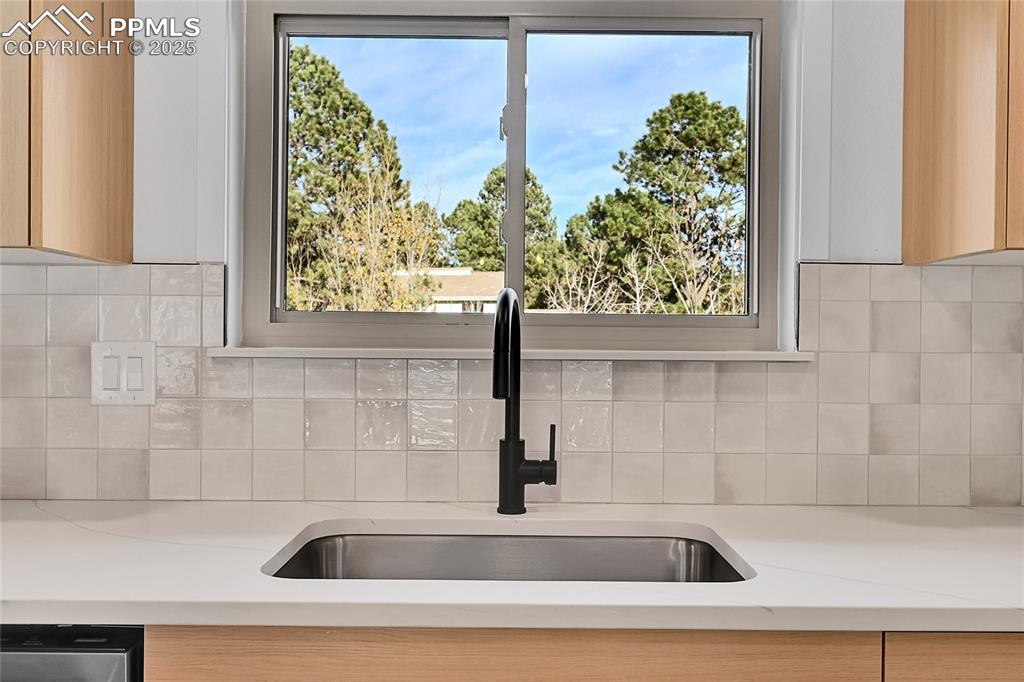 Image 15 of 40: Kitchen view of tasteful backsplash, light brown cabinetry, and light stone