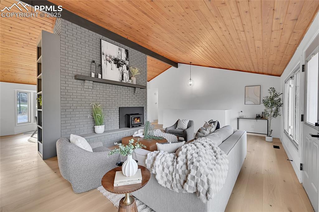 Image 18 of 40: Living area with wooden ceiling, light wood finished floors, and a brick fi