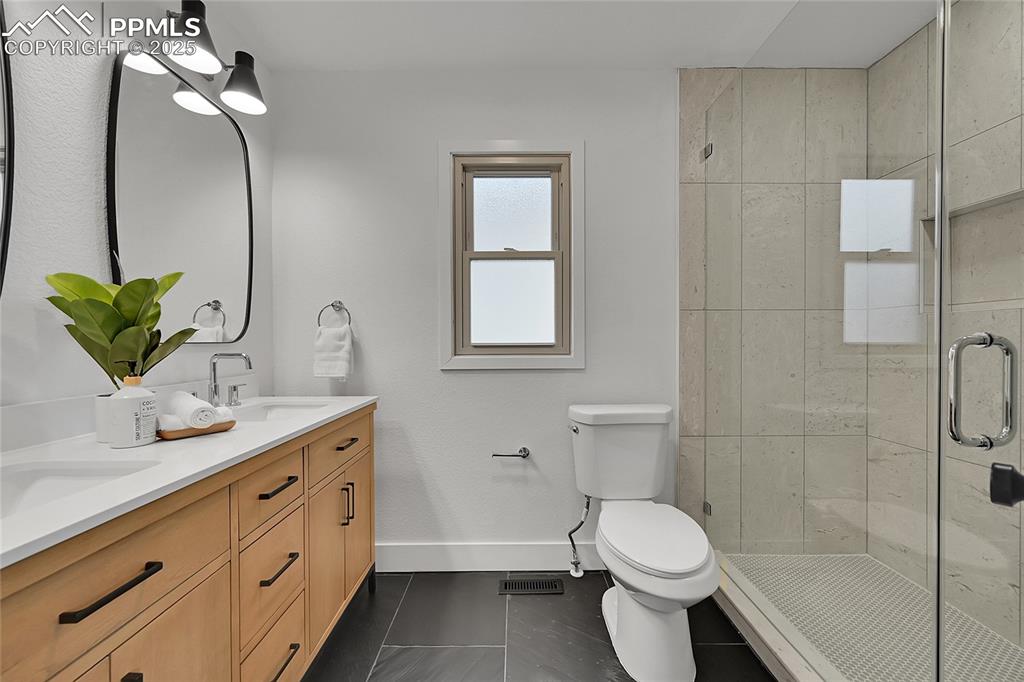 Image 25 of 40: Bathroom featuring double vanity, a stall shower, and dark tile patterned f