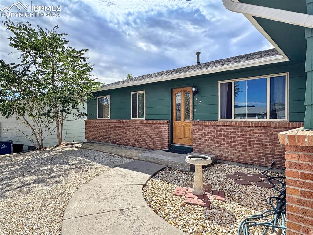 Image 2 of 8: Doorway to property featuring brick siding and roof with shingles