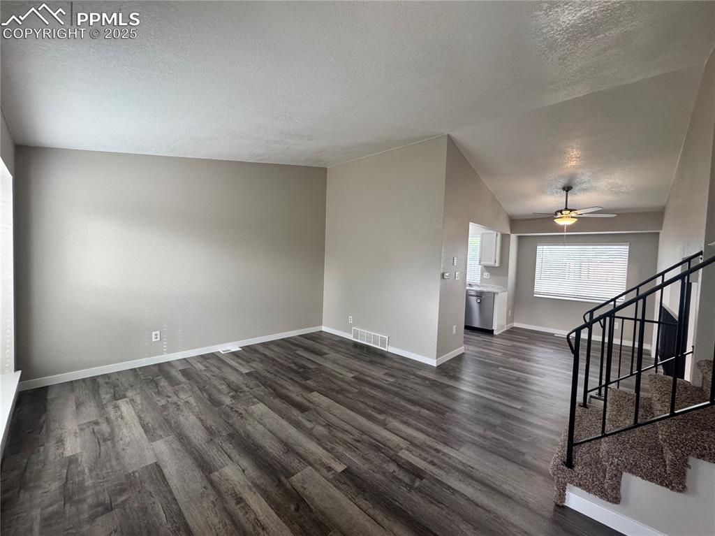 Image 15 of 24: Unfurnished living room with a textured ceiling, stairway, dark wood finish