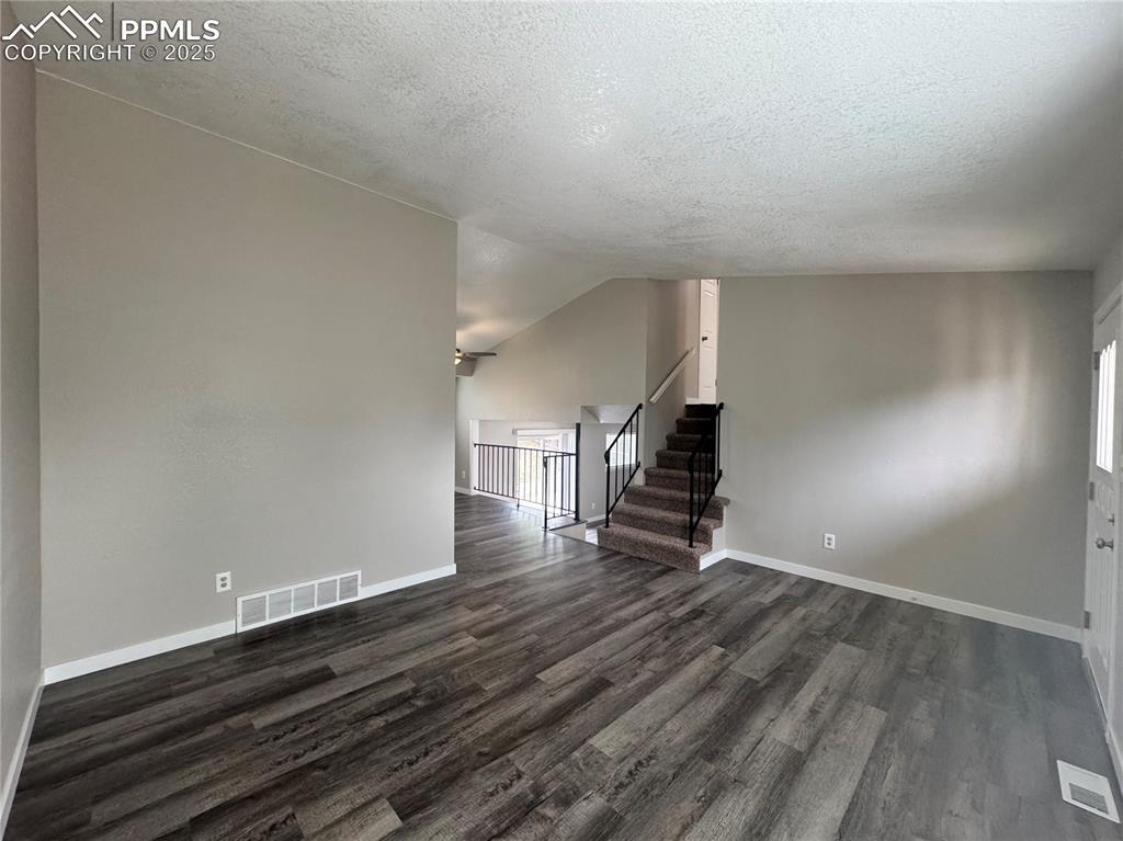 Image 16 of 24: Unfurnished living room featuring stairs, dark wood-type flooring, a textur