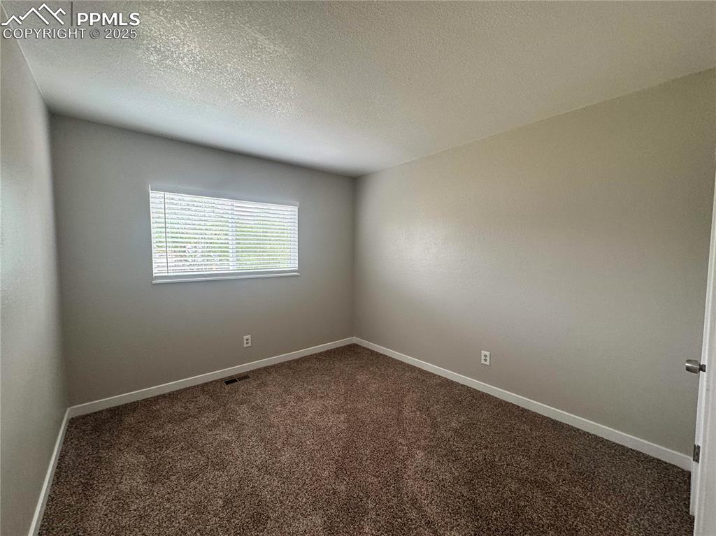 Image 22 of 24: Carpeted empty room with a textured ceiling and baseboards