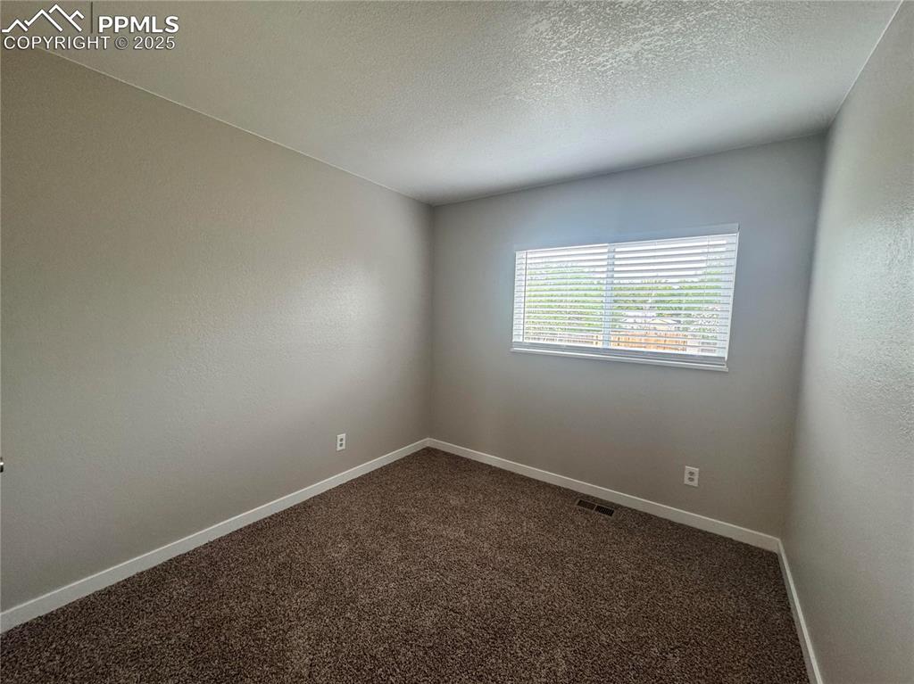 Image 23 of 24: Empty room with dark colored carpet and a textured ceiling