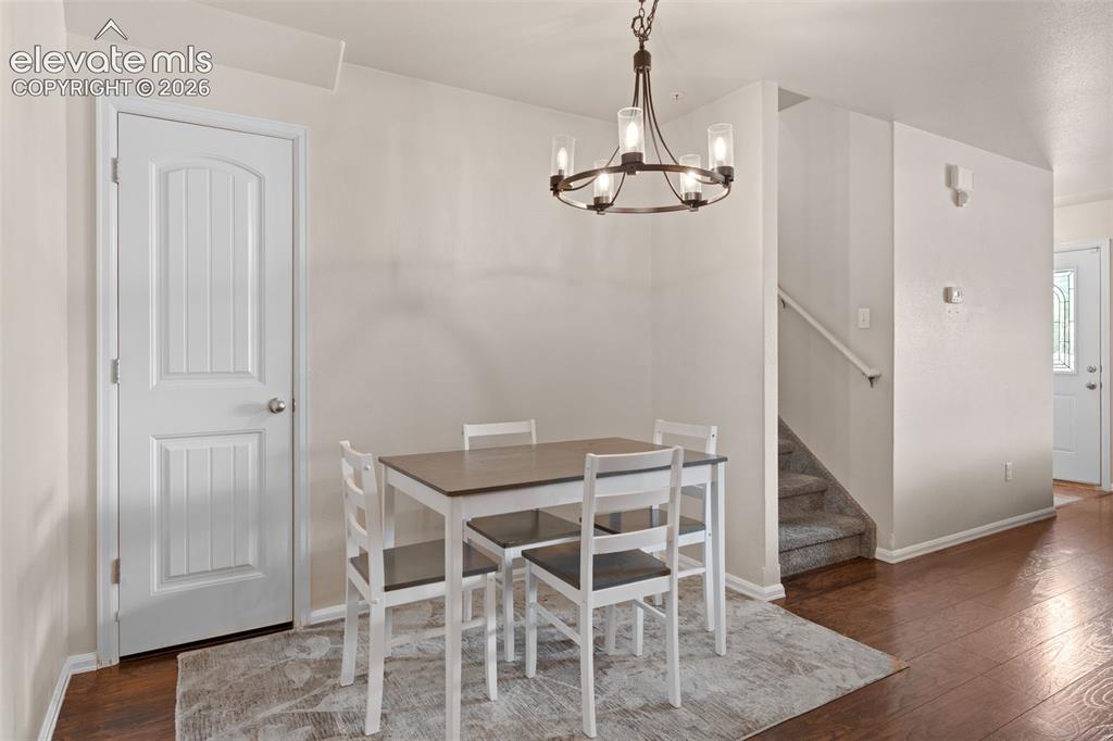 Image 14 of 32: Wood-finish flooring with a multi-light chandelier and white paneled interi