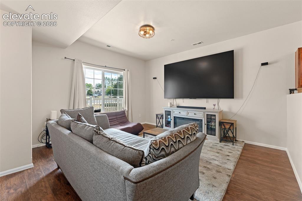 Image 8 of 32: Spacious living area featuring wood-finish flooring, a wall-mounted enterta