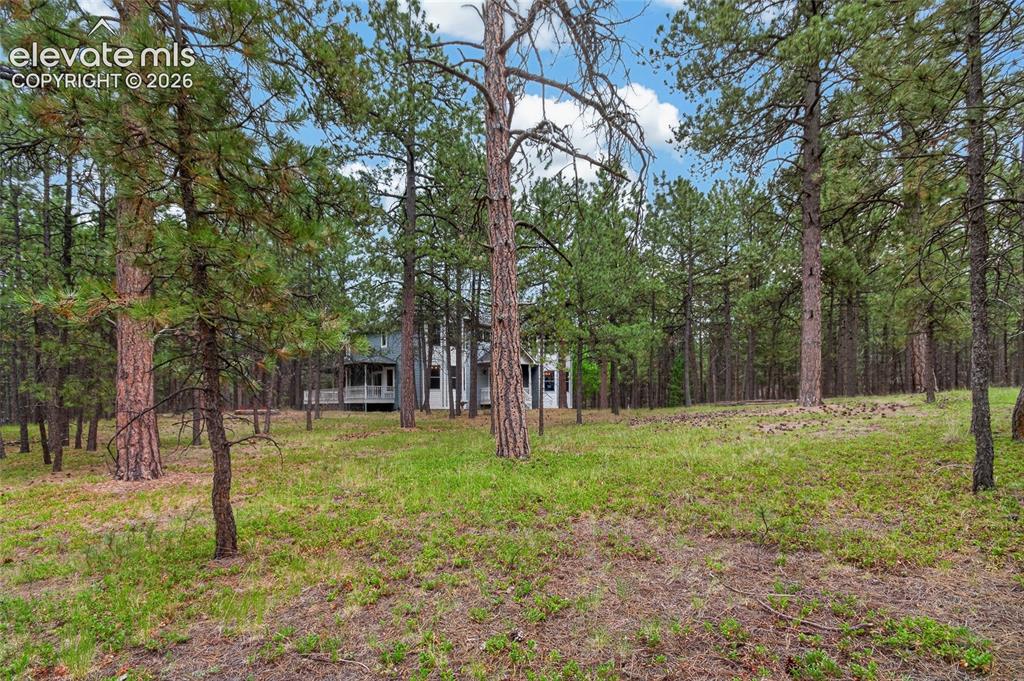 Image 8 of 46: Wooded property featuring a large home with a covered porch and balcony, se