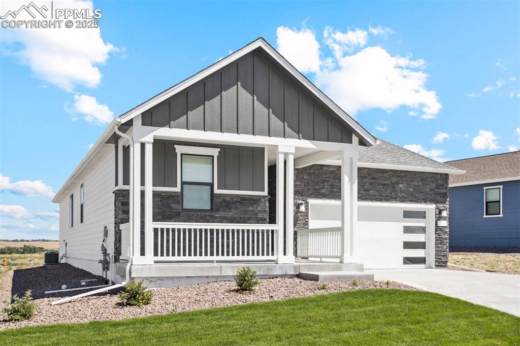 Caption: View of front of property with stone siding, board and batten siding, driveway, a porch, and a garag