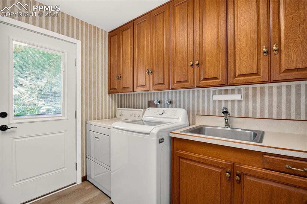 Image 25 of 43: Washroom with wallpapered walls, cabinet space, washing machine and dryer, 