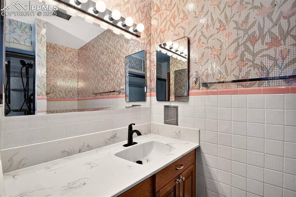 Image 27 of 43: Bathroom featuring wallpapered walls, vanity, and tile walls