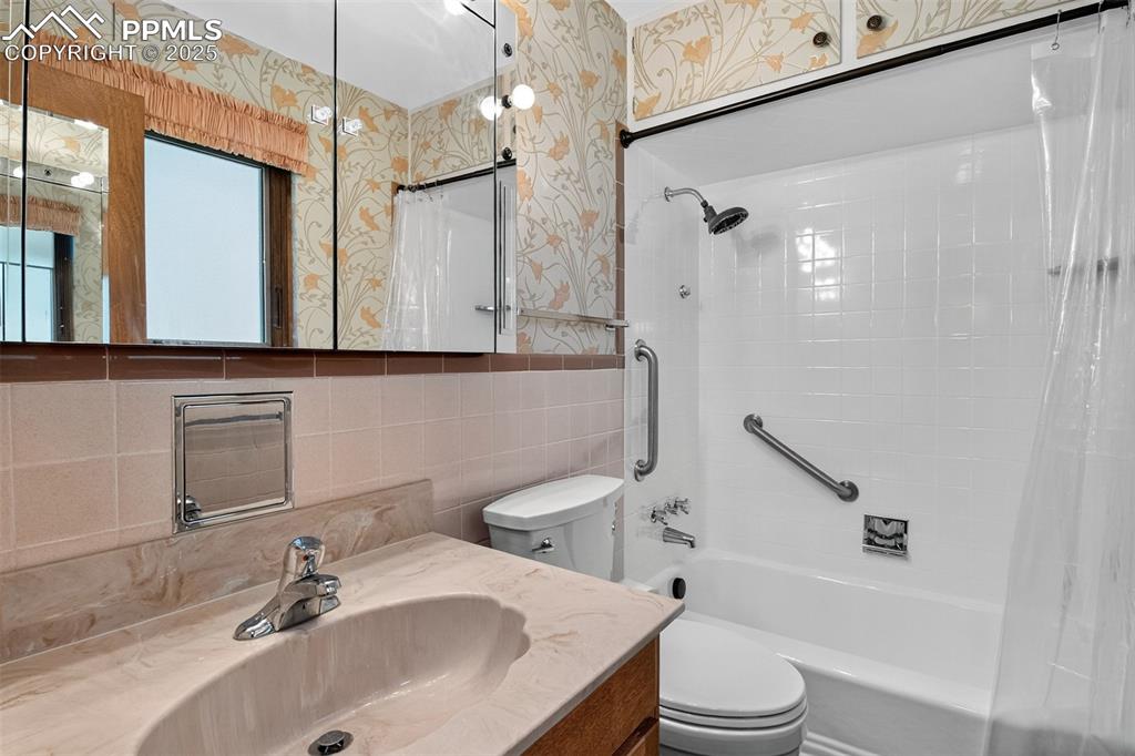 Image 28 of 43: Bathroom with wallpapered walls, shower / bathtub combination with curtain,