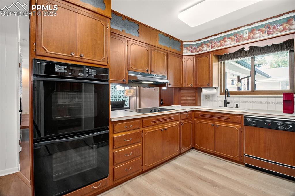 Image 3 of 43: Kitchen with brown cabinetry, dishwasher, light wood-style flooring, and li