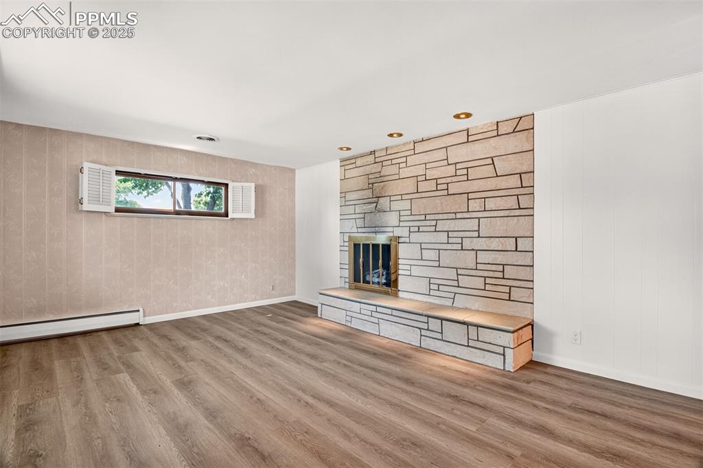 Image 5 of 43: Unfurnished living room featuring wood finished floors, a stone fireplace, 