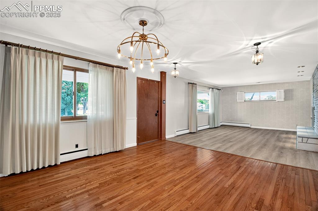 Image 6 of 43: Unfurnished living room with a chandelier, wood finished floors, and a base