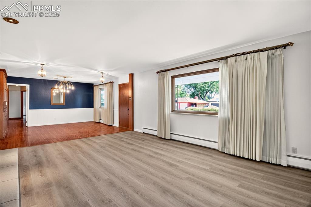 Image 9 of 43: Unfurnished living room featuring wood finished floors, a chandelier, a bas