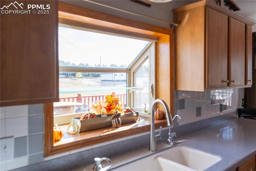 Image 19 of 49: Kitchen with decorative backsplash, dark countertops, and brown cabinetry