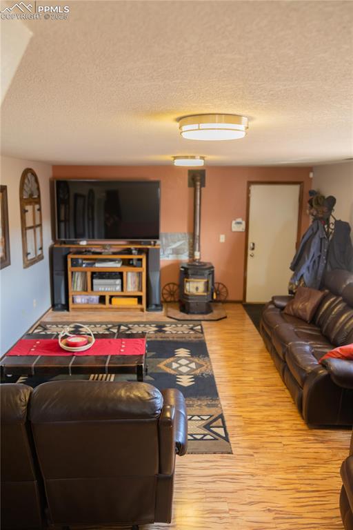 Image 22 of 49: Living area with wood finished floors, a textured ceiling, and a wood stove