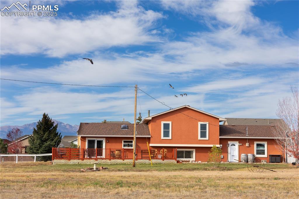 Image 6 of 49: Back of property with a wooden deck, stucco siding, a yard, and a shingled