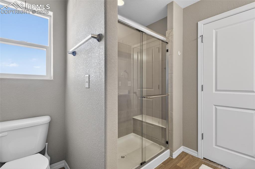 Image 21 of 38: Full bathroom with a shower stall, a textured wall, and wood finished floor