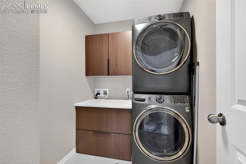 Image 25 of 38: Laundry room featuring a textured wall, stacked washing machine and dryer, 