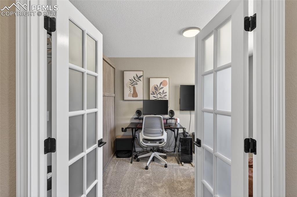 Image 28 of 38: Office space with french doors, light colored carpet, and a textured ceilin