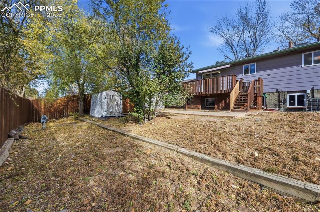 Image 23 of 26: Fenced backyard featuring a wooden deck, a storage shed, and stairway