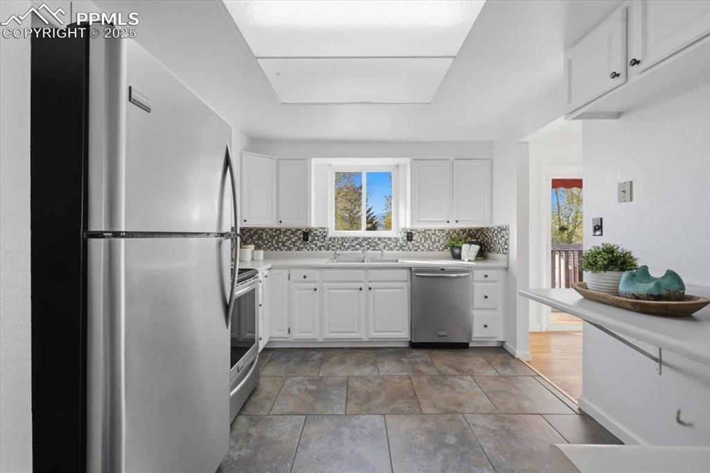 Image 8 of 26: Kitchen featuring stainless steel appliances, white cabinets, backsplash, a