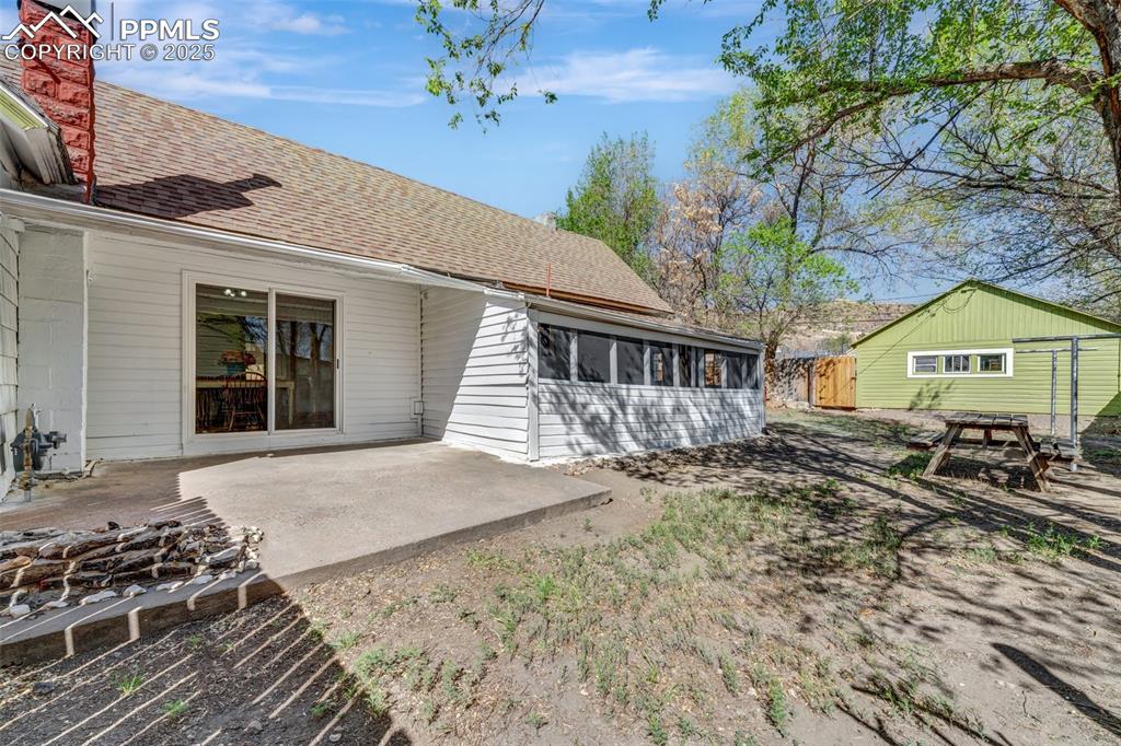 Image 23 of 34: Screened in Porch, Cement Patio, and Green Garage in Background