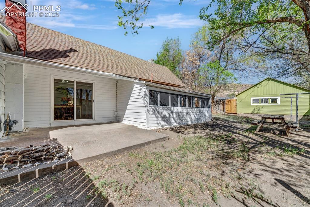 Image 23 of 34: Screened in Porch, Cement Patio, and Green Garage in Background