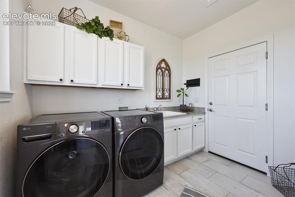 Image 16 of 46: Functional laundry space featuring light-toned flooring, white cabinetry, a