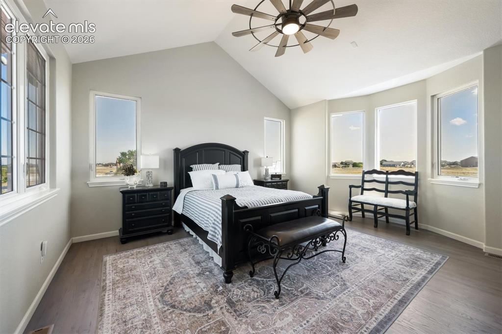 Image 17 of 46: Vaulted ceiling bedroom with multiple windows, a ceiling fan, and wood-fini