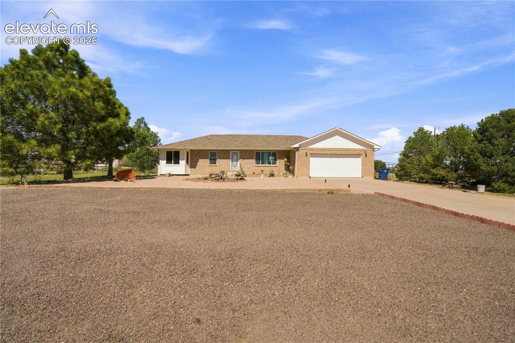Caption: Brick exterior with an attached garage, pitched roof, and mature trees