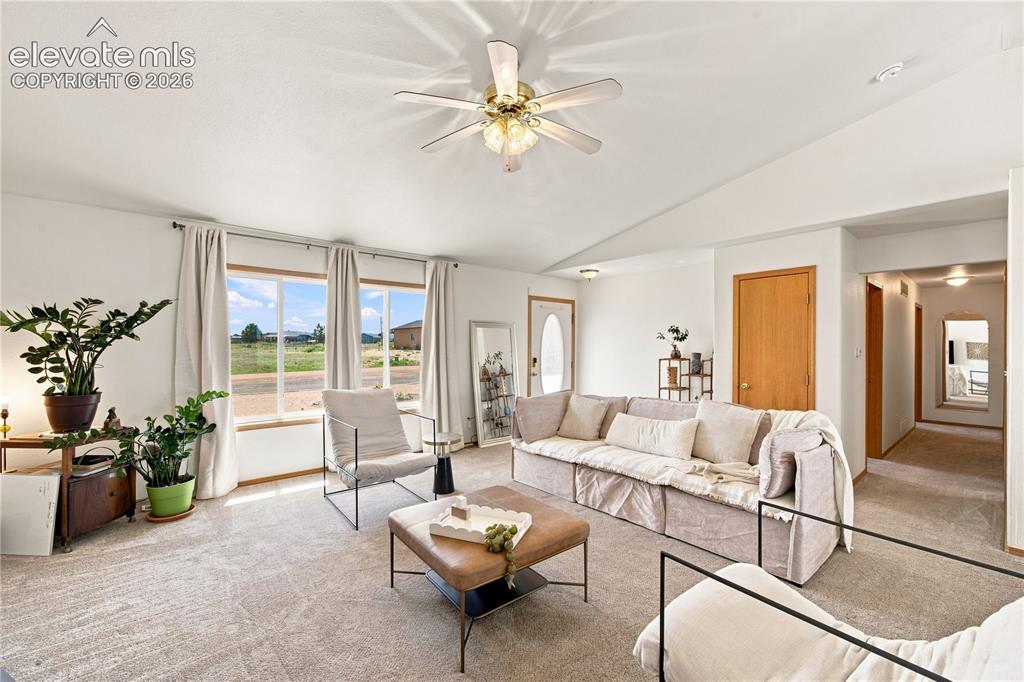 Image 2 of 37: Vaulted ceiling with a ceiling fan, light-toned carpeting, and a series of 