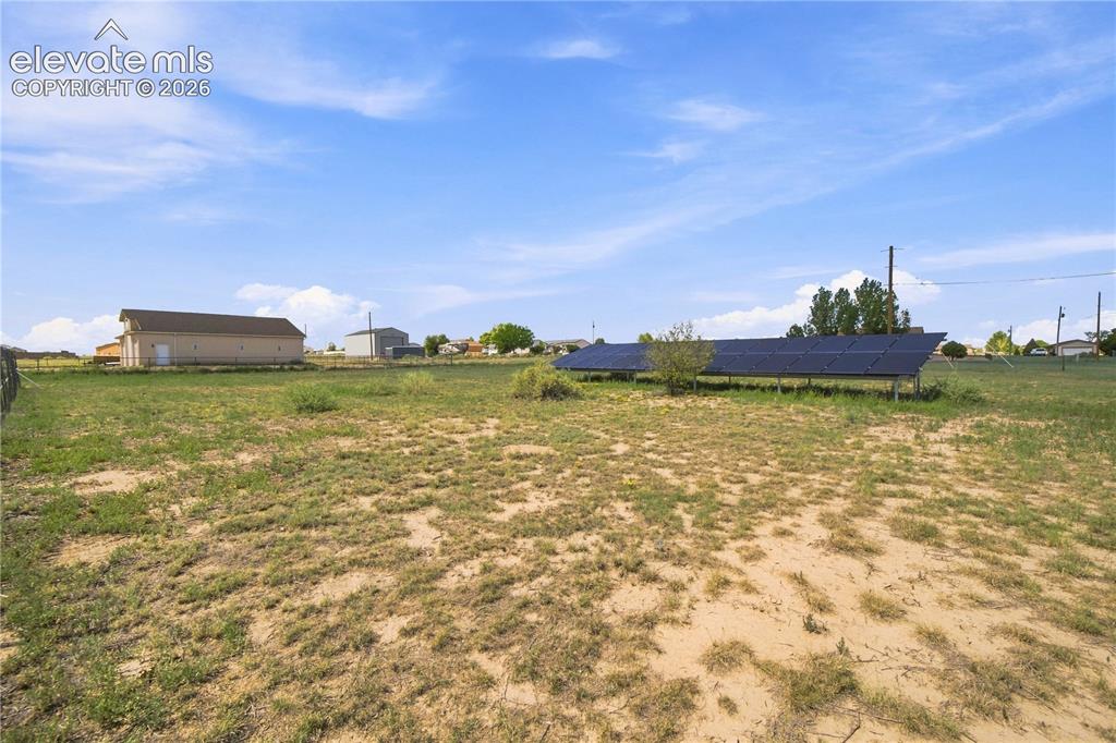 Image 30 of 37: Expansive open land featuring solar panel arrays and a detached utility bui