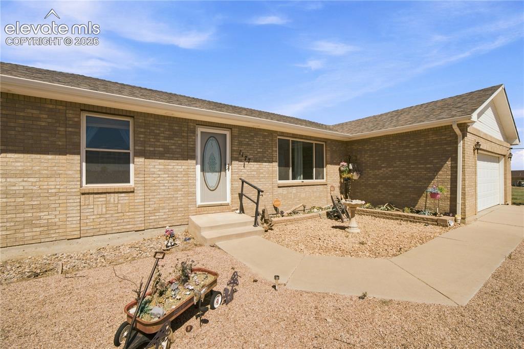 Image 31 of 37: Brick exterior with a covered entryway, attached two-car garage, and a conc