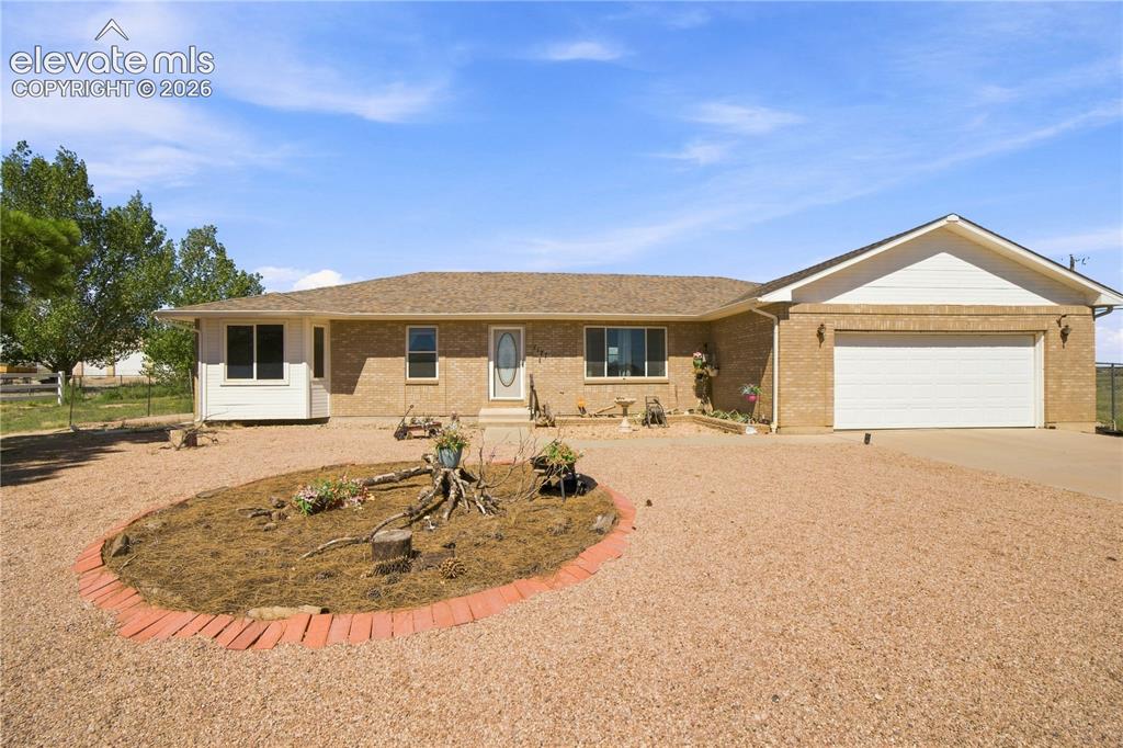 Image 32 of 37: Brick exterior with a two-car garage, gravel driveway, and a bay window
