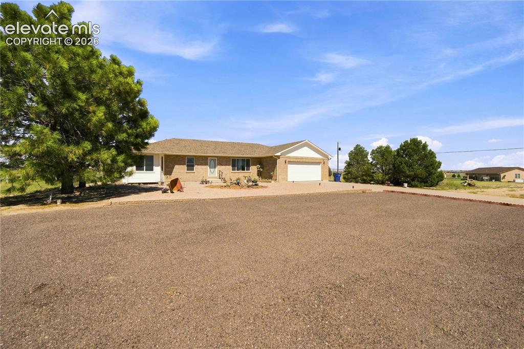 Image 34 of 37: Brick exterior with an attached garage, paved driveway, and mature landscap