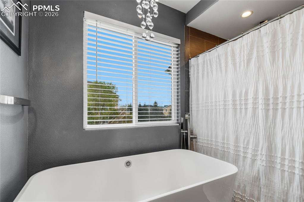 Image 24 of 43: Bathroom featuring a freestanding white bathtub, a window with horizontal b