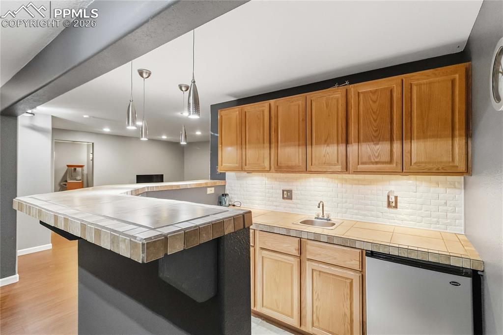 Image 34 of 43: Entertainment area featuring a tiled wraparound bar, overhead pendant light