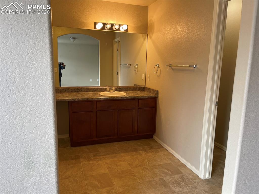 Image 13 of 15: Bathroom vanity featuring a single basin sink, laminate countertop, and woo