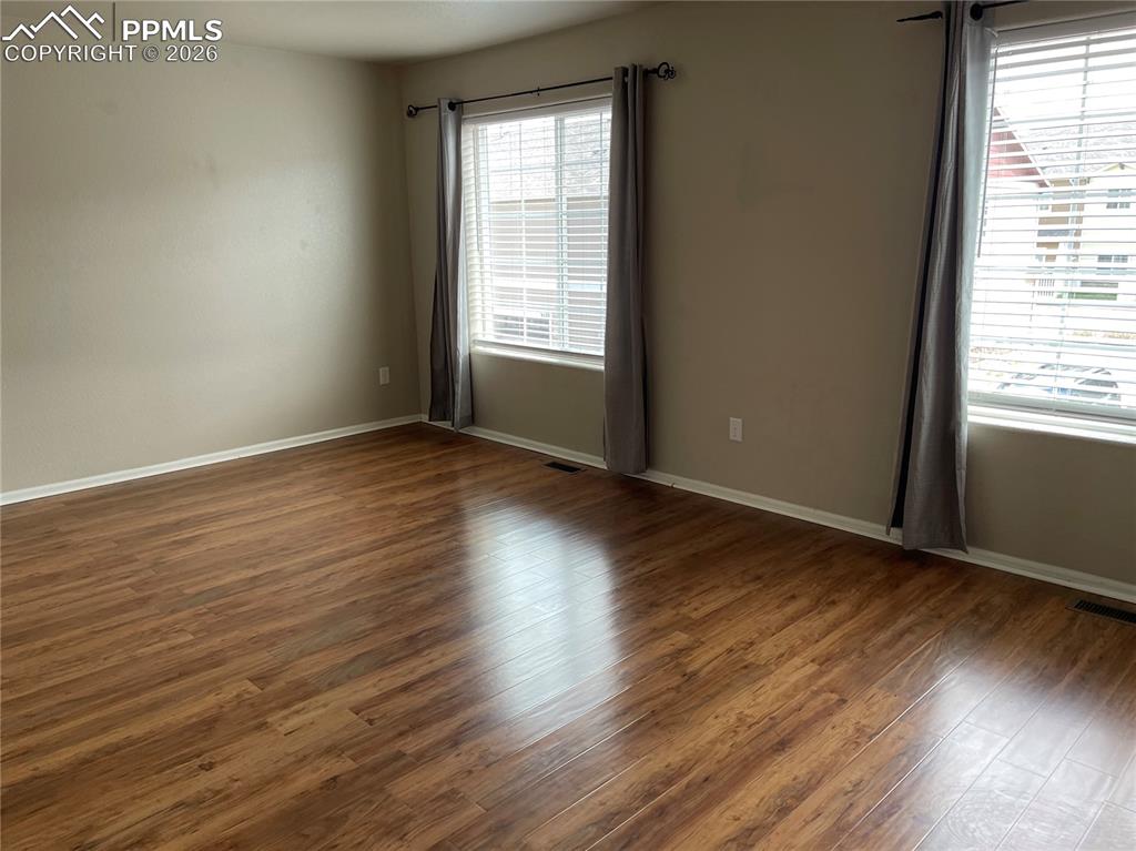 Image 9 of 15: Spacious interior featuring wood-finish flooring, two large windows with bl