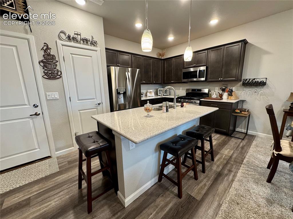 Image 10 of 25: Kitchen featuring dark-toned cabinetry, light-colored stone-finish countert