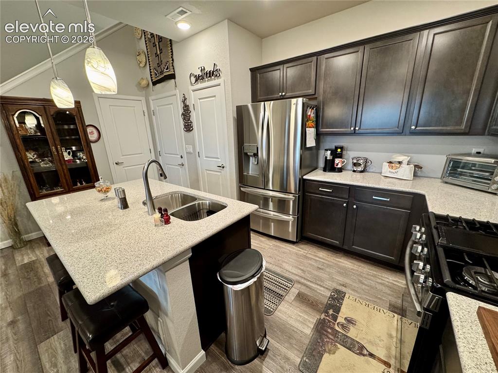 Image 2 of 25: Kitchen featuring dark wood cabinetry, light-toned stone countertops, a cen