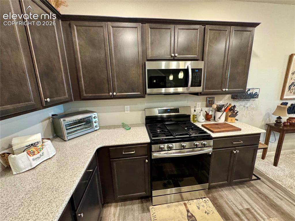 Image 8 of 25: Kitchen featuring dark-toned cabinetry, light-colored countertops, stainles