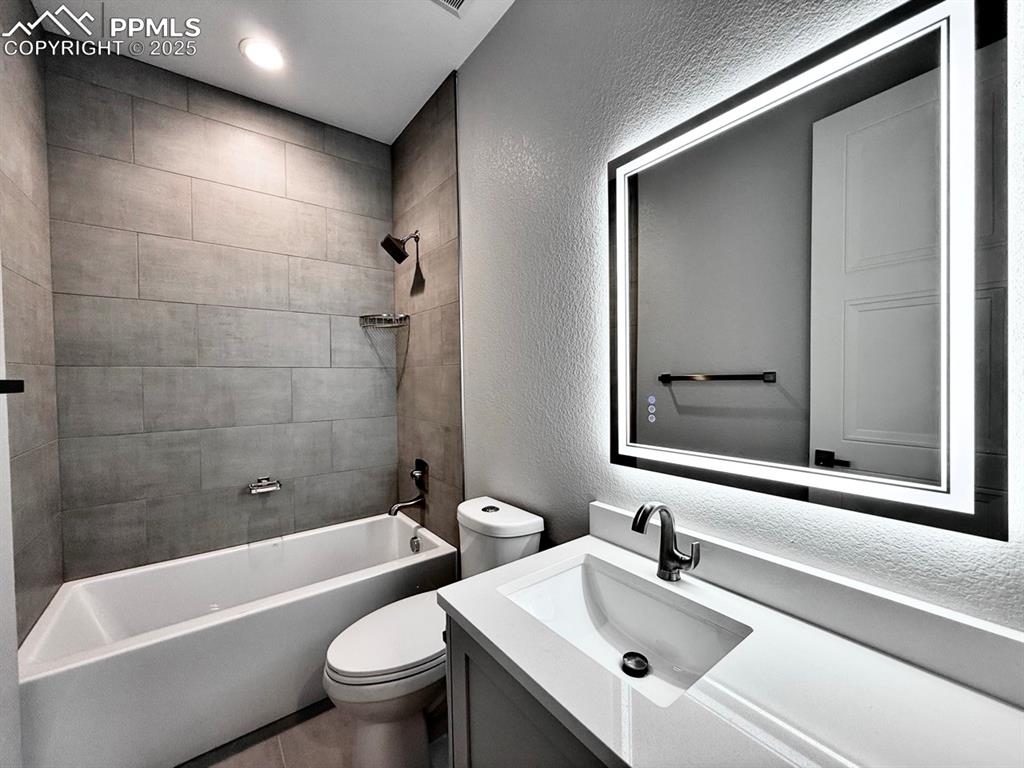 Image 5 of 28: Bathroom featuring a textured wall, shower / bathtub combination, vanity, a