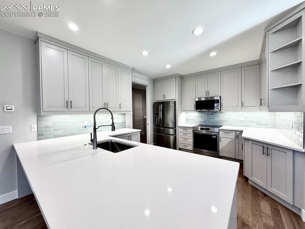 Image 9 of 28: Kitchen with open shelves, stainless steel appliances, decorative backsplas